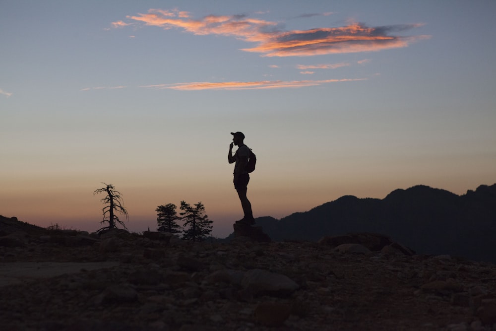 silhouette dell'uomo in piedi su terreno roccioso durante il tramonto