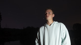 A model wearing mocsy’s signature dark hoodie standing against a starry night backdrop