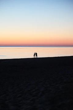 A cinematic portrait of a couple sharing a quiet moment by the beach at sunset.