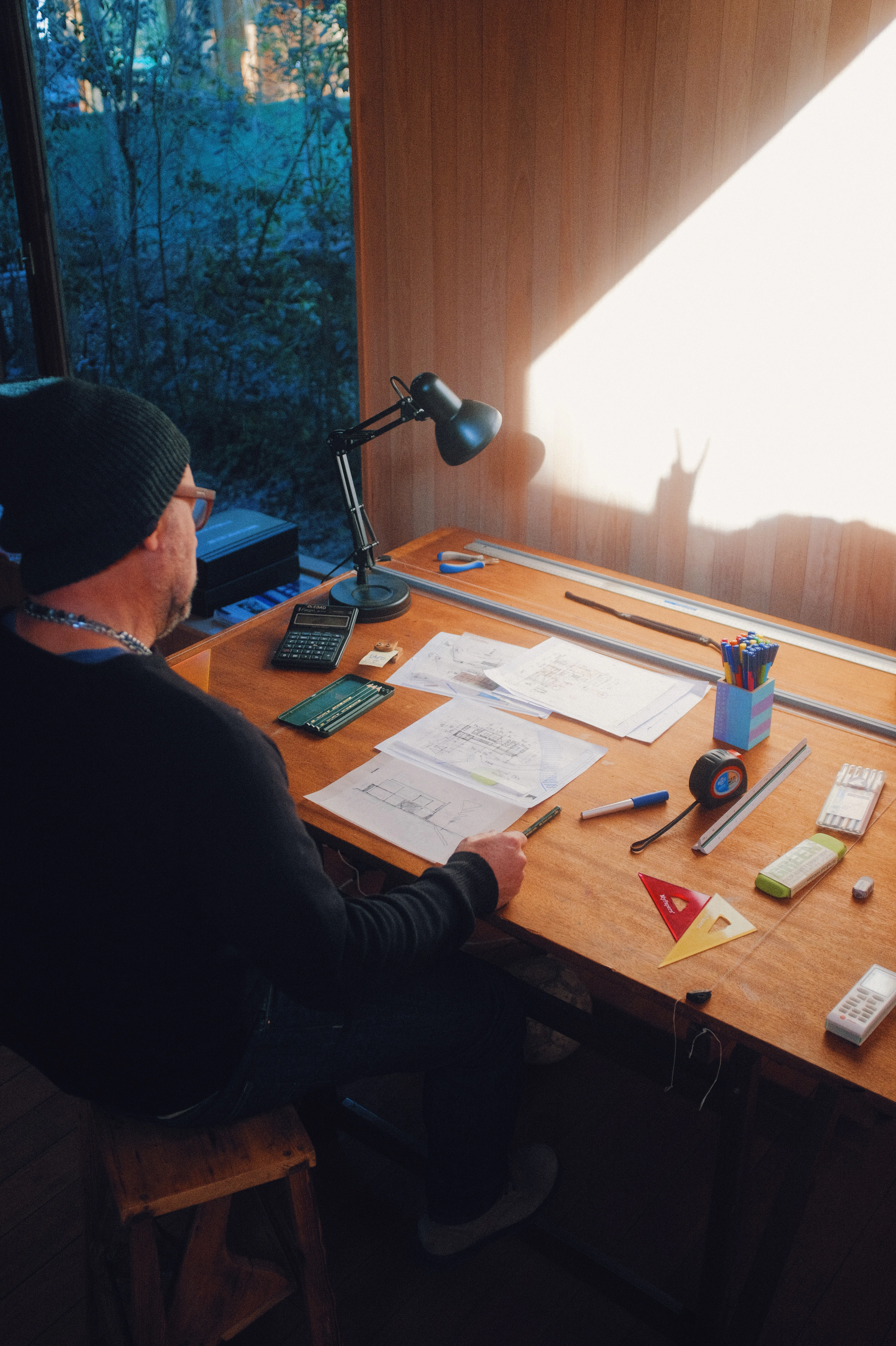 Drafting table in the studio with drawings, scale rulers and a lamp in late-afternoon light