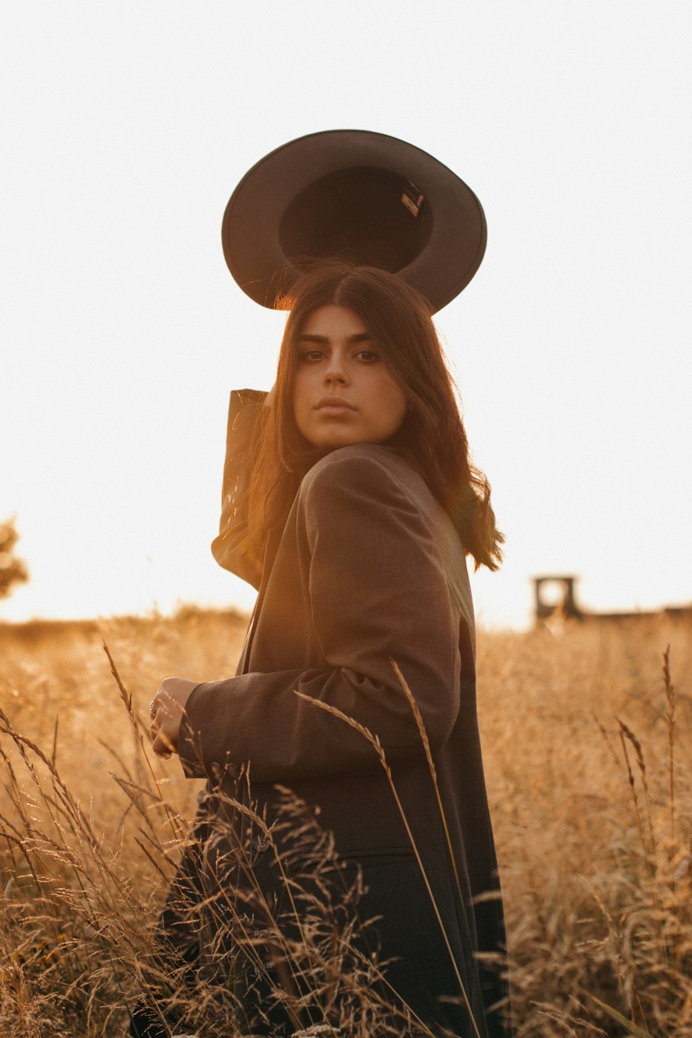 woman in brown coat wearing black hat standing on brown grass field during daytime