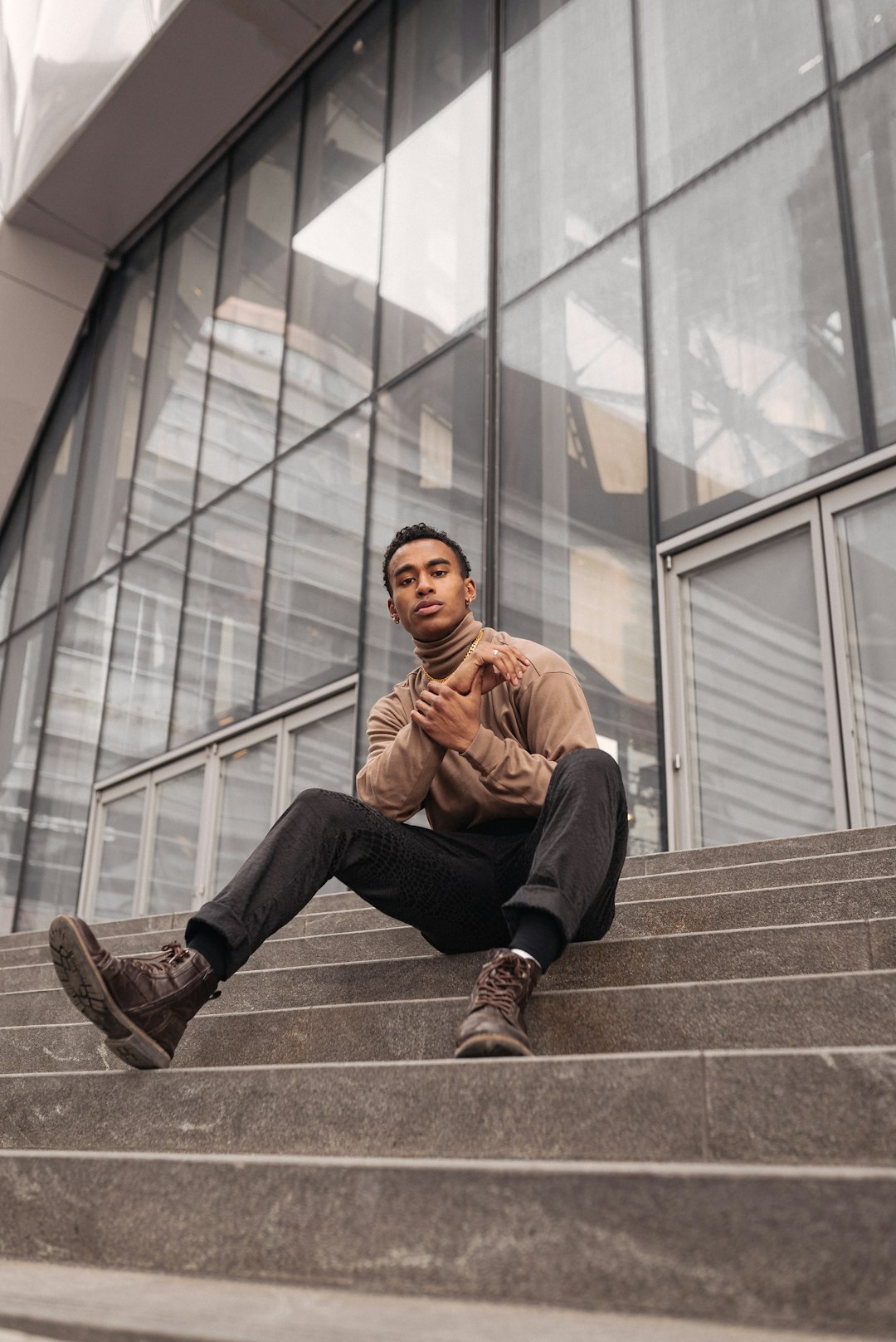 man in brown jacket and black pants sitting on brown concrete stairs