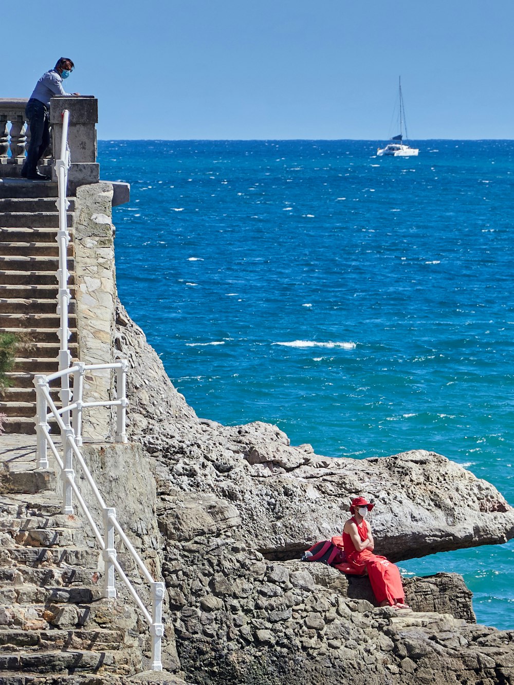 woman in red dress sitting on gray concrete stairs near blue sea during daytime