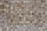 A close-up view of a textured wall composed of small rectangular stone tiles arranged in a grid pattern. The colors of the tiles vary, featuring different shades of brown, beige, and gray. The surface shows natural stone patterns with slight variations in texture and appearance.