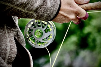Hands adjusting a fishing rod in a bright, organized workshop