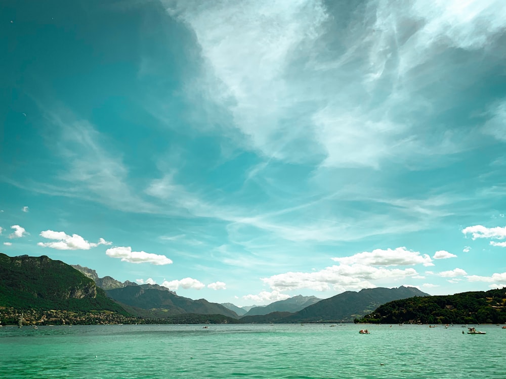 green mountains beside body of water under blue sky and white clouds during daytime