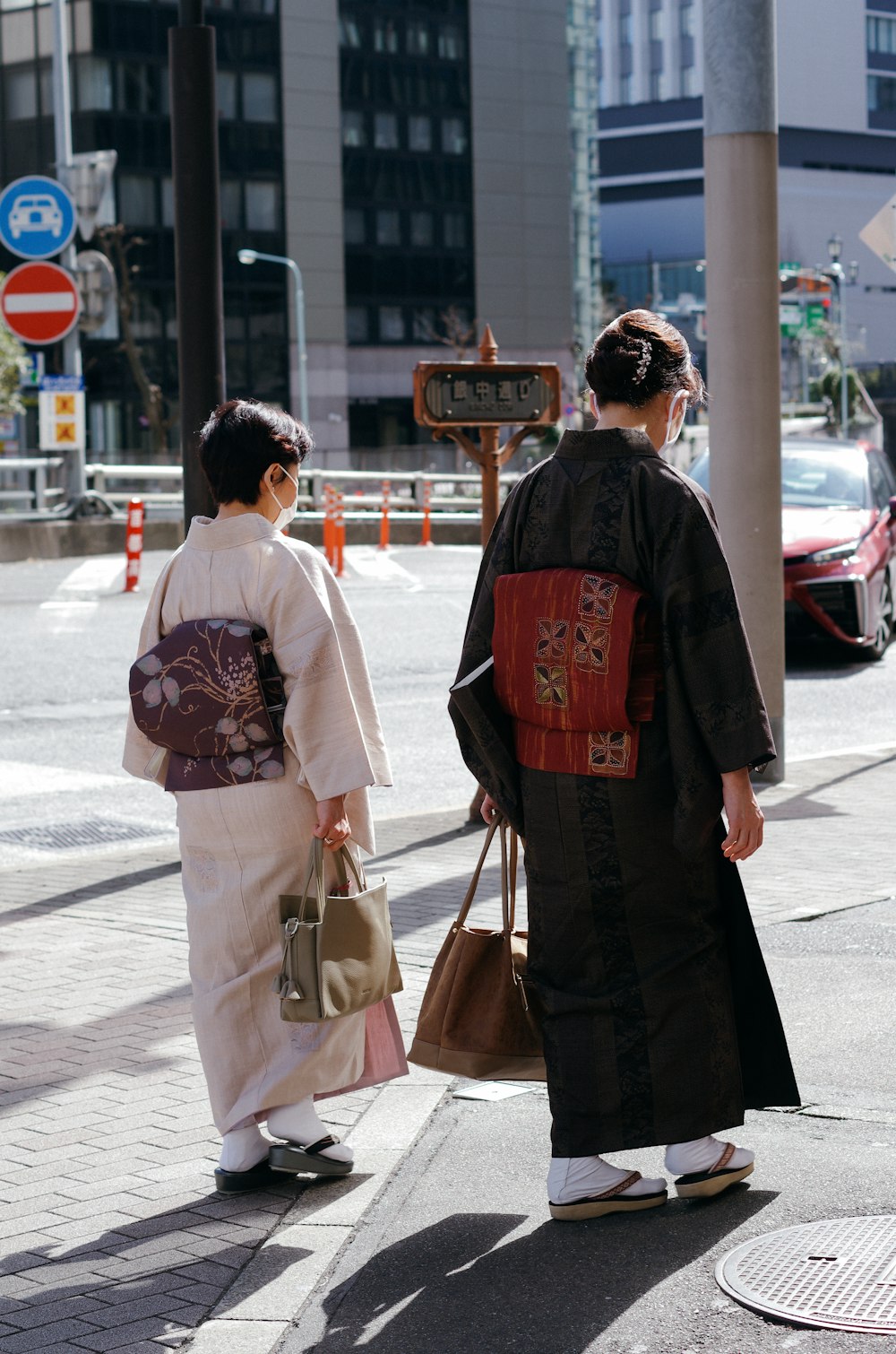 2 women in kimono standing on sidewalk during daytime
