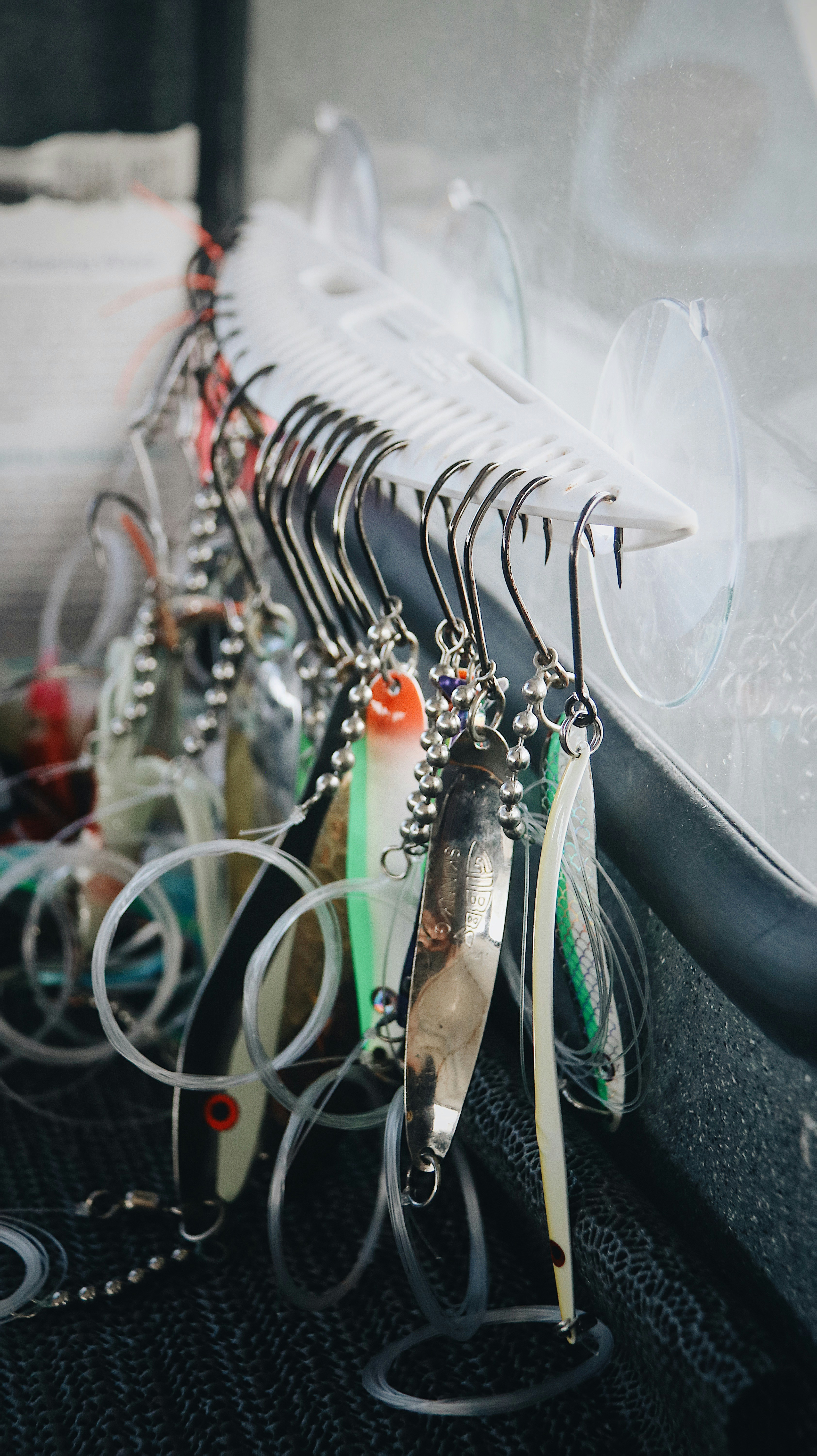 Rigged trolling lures with steel hooks and bead chain hanging in a row inside a boat, a clear plastic sheet behind them