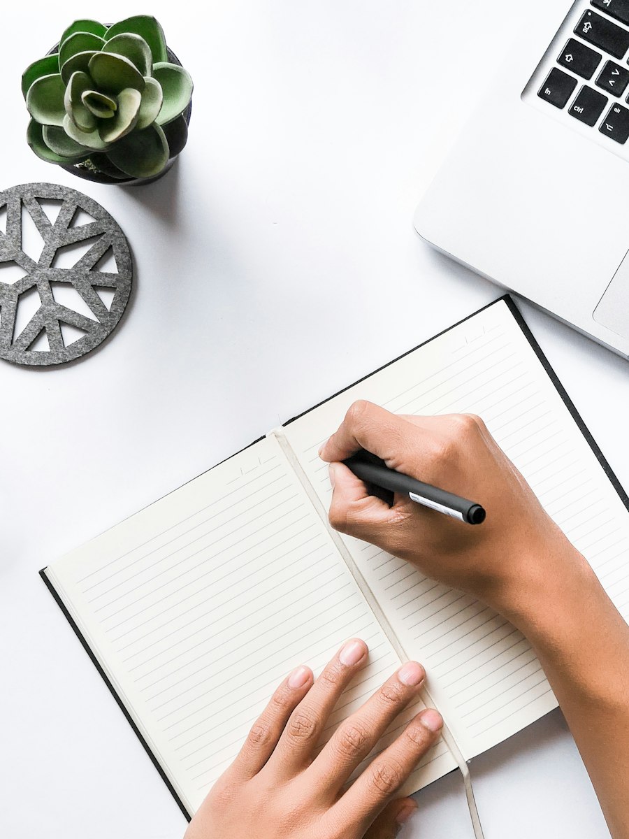 Hands writing in a notebook beside a laptop