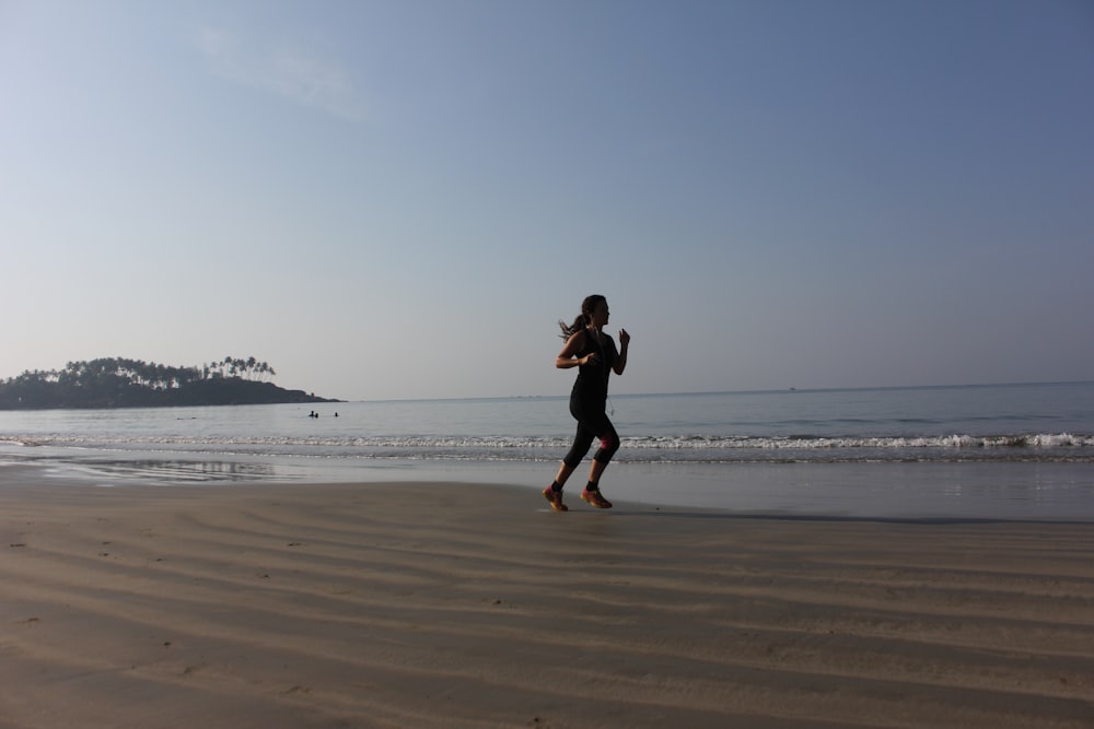mujer en vestido negro corriendo en la playa durante el día