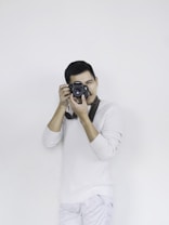 man in white sweater holding black dslr camera