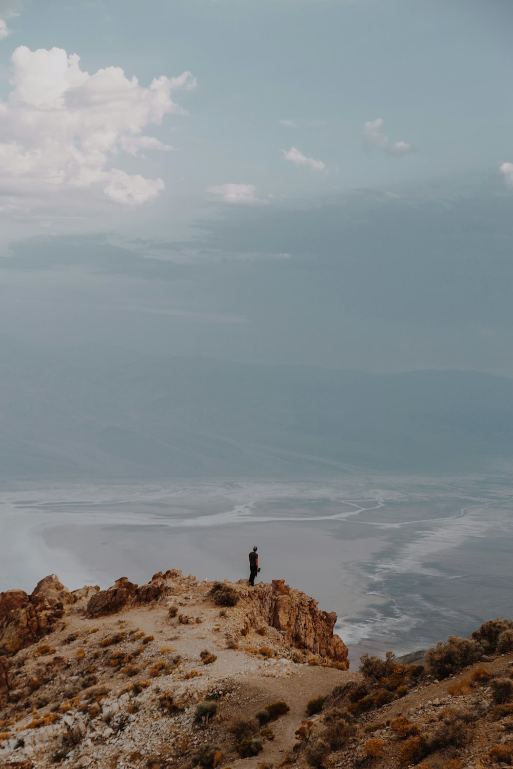 person standing on brown rock formation under white clouds during daytime