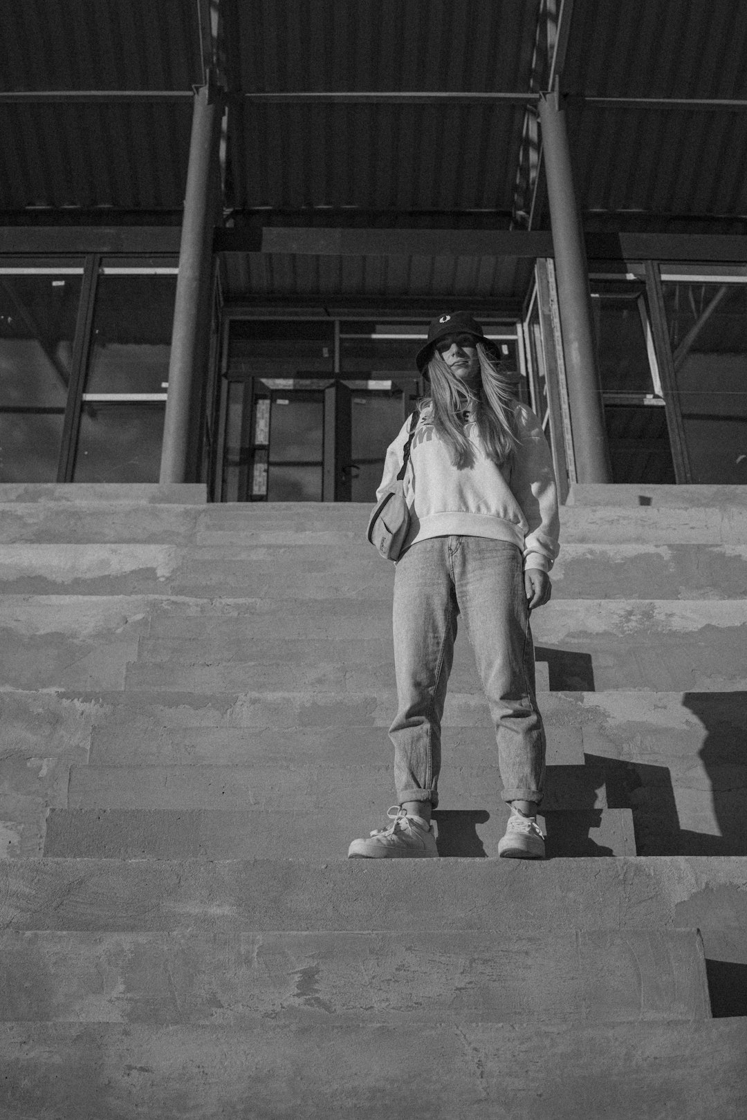 grayscale photo of woman in long sleeve shirt and pants standing on concrete stairs
