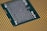 A close-up of a computer processor with numerous small metallic components and gold contact pins on a green substrate. The focus is on the central section with detailed circuitry, surrounded by a grid pattern of contacts.
