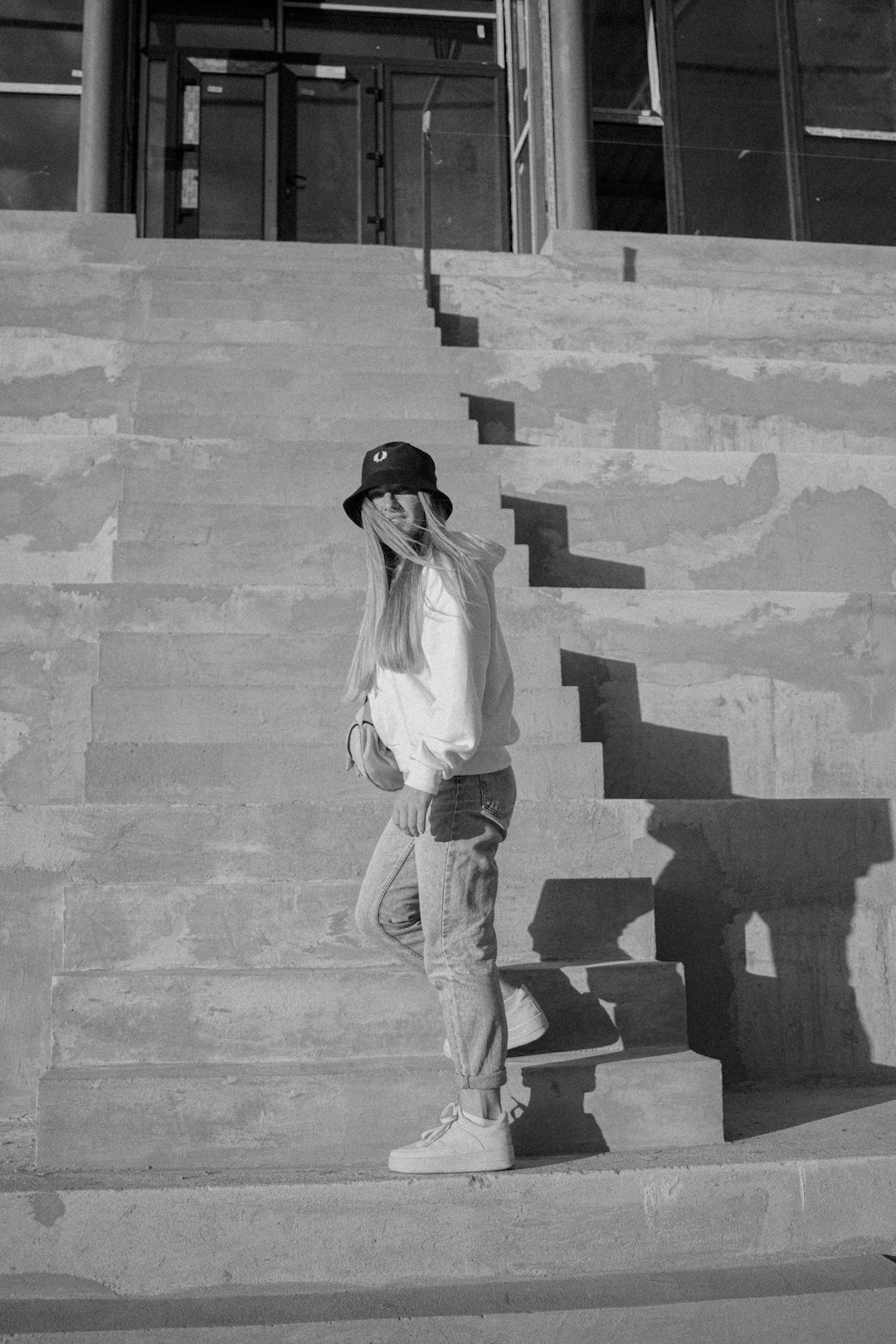 grayscale photo of woman in white long sleeve shirt and brown pants standing on concrete stairs