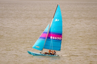 man in black shirt riding on blue and white sail boat on sea during daytime