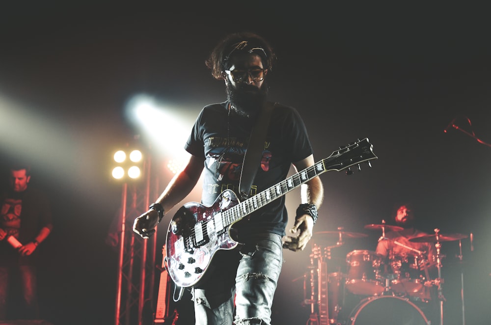 Hombre con camiseta negra de cuello redondo tocando la guitarra eléctrica