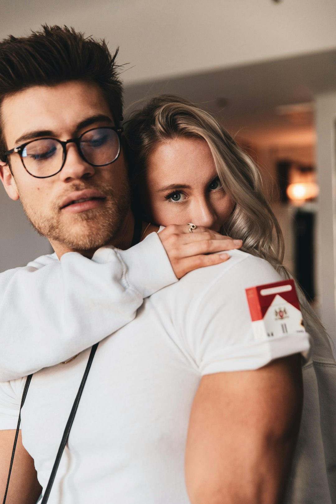 man in white polo shirt and black framed eyeglasses hugging woman in white t-shirt