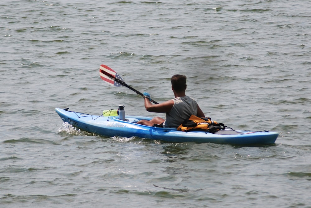 man in orange jacket riding blue kayak on body of water during daytime