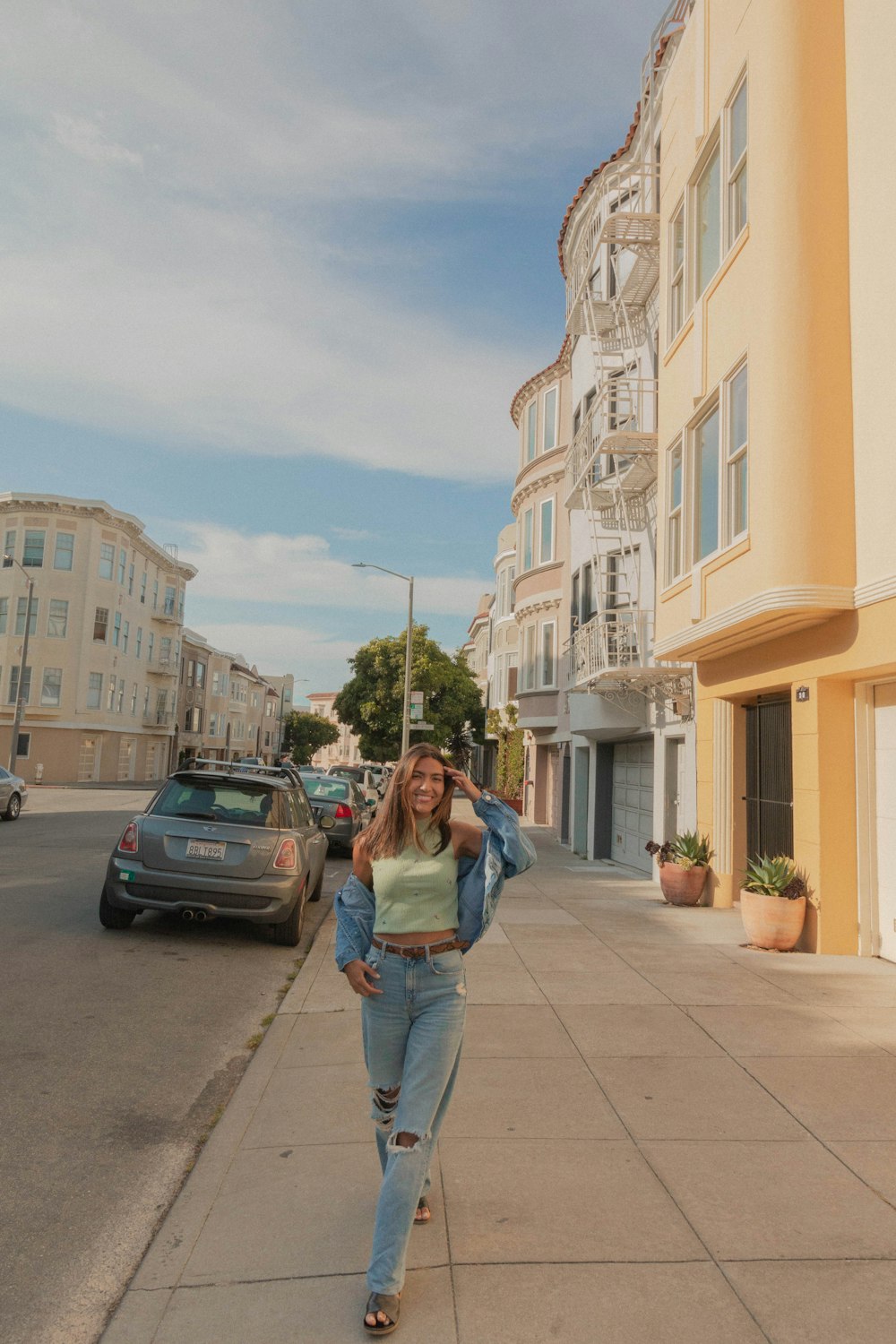 woman in blue denim jacket and blue denim jeans standing on sidewalk during daytime