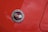 A close-up view of an emblem with the text 'Chevrolet Motor Division Corvette' featuring two crossed flags on a glossy red car surface with water droplets scattered across.