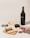 A bottle of red wine labeled 'ONDULÉ NAPA VALLEY CALIFORNIA 2013' is positioned next to a glass of wine and a selection of cheeses and crackers on a wooden board. A person's hand with pink nail polish is holding a cracker. A corkscrew and cork are visible, both branded with 'ONDULÉ'. The setting suggests a casual wine and cheese tasting.