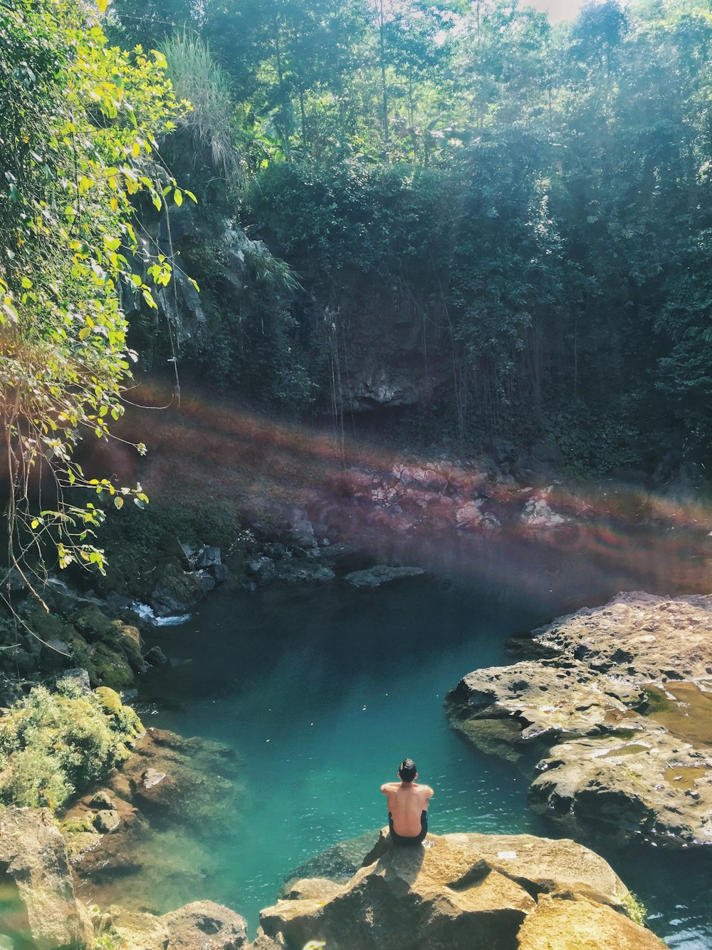 person in blue shorts standing on rock near river during daytime