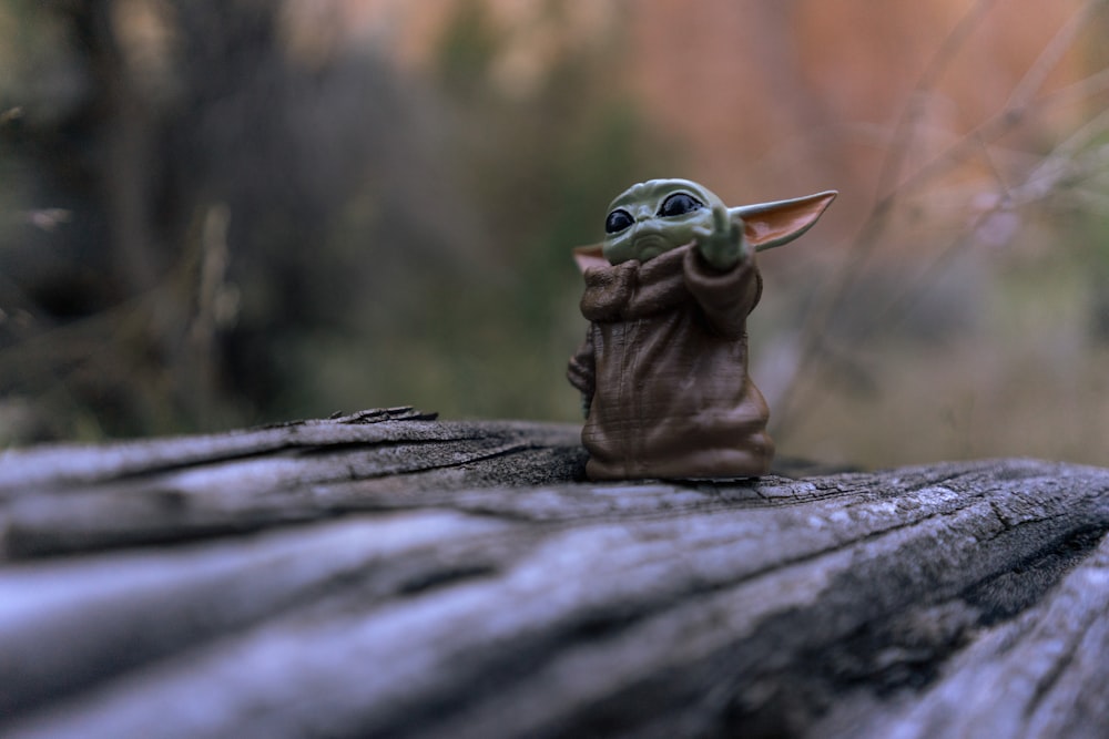 Una statuetta di Baby Yoda seduta sopra un tronco