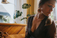 A happy woman admiring her noorzar earrings in a sunlit room.