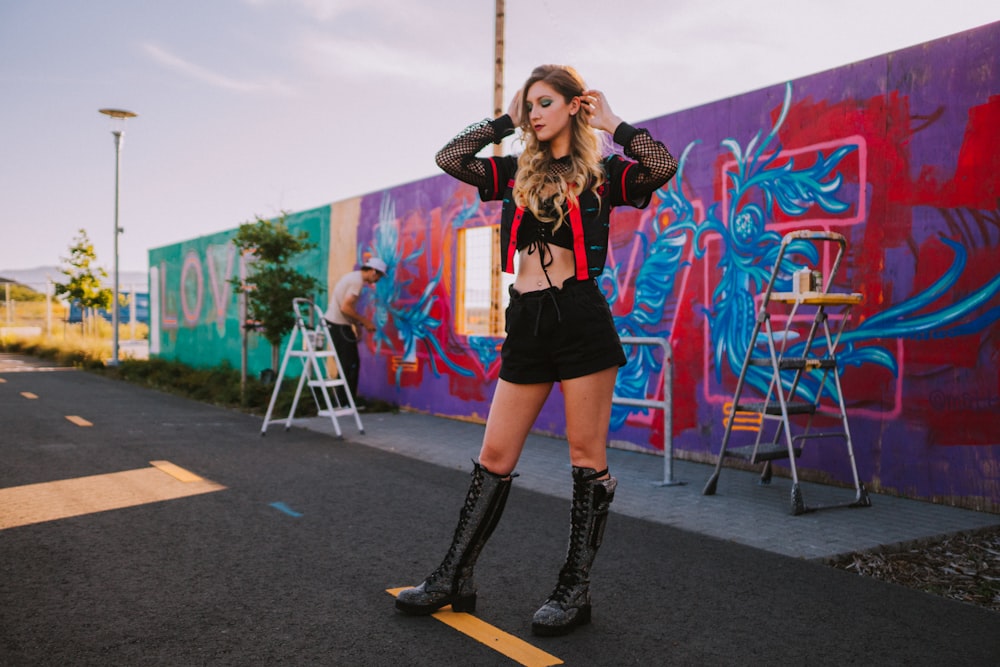 woman in black jacket and blue denim jeans standing on black asphalt road during daytime