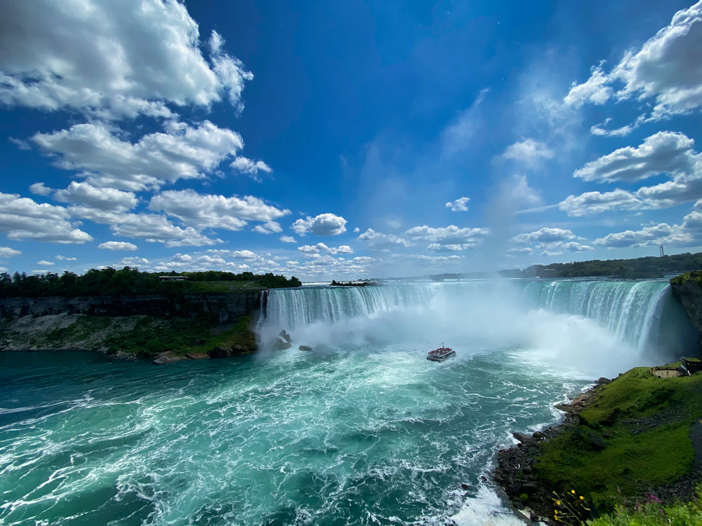 Horseshoe Falls at Niagara with the full sweep of the Canadian Horseshoe visible, mist rising, and the Maid of the Mist tour boat below against the turquoise water