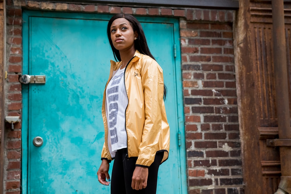 woman in yellow jacket standing beside blue wall