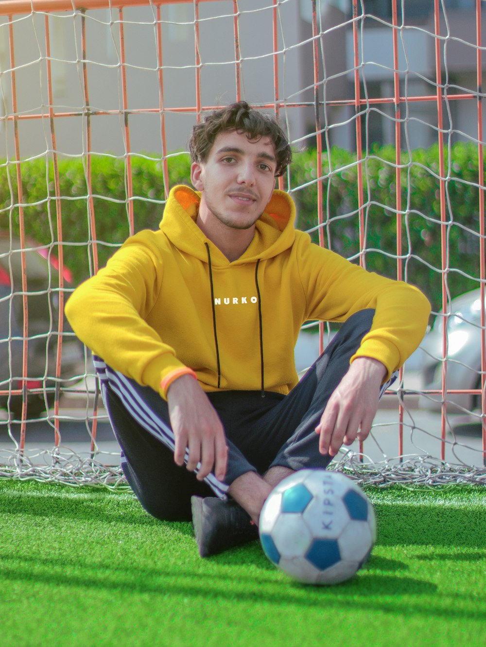 boy in yellow sweater and black pants sitting on soccer goal net