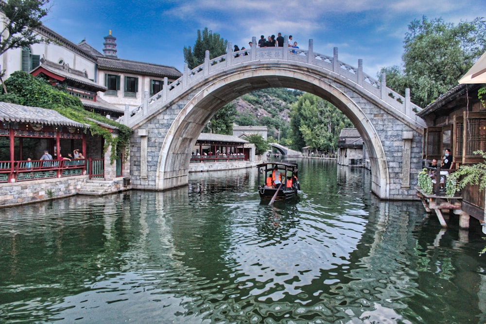 people riding boat on river under bridge during daytime