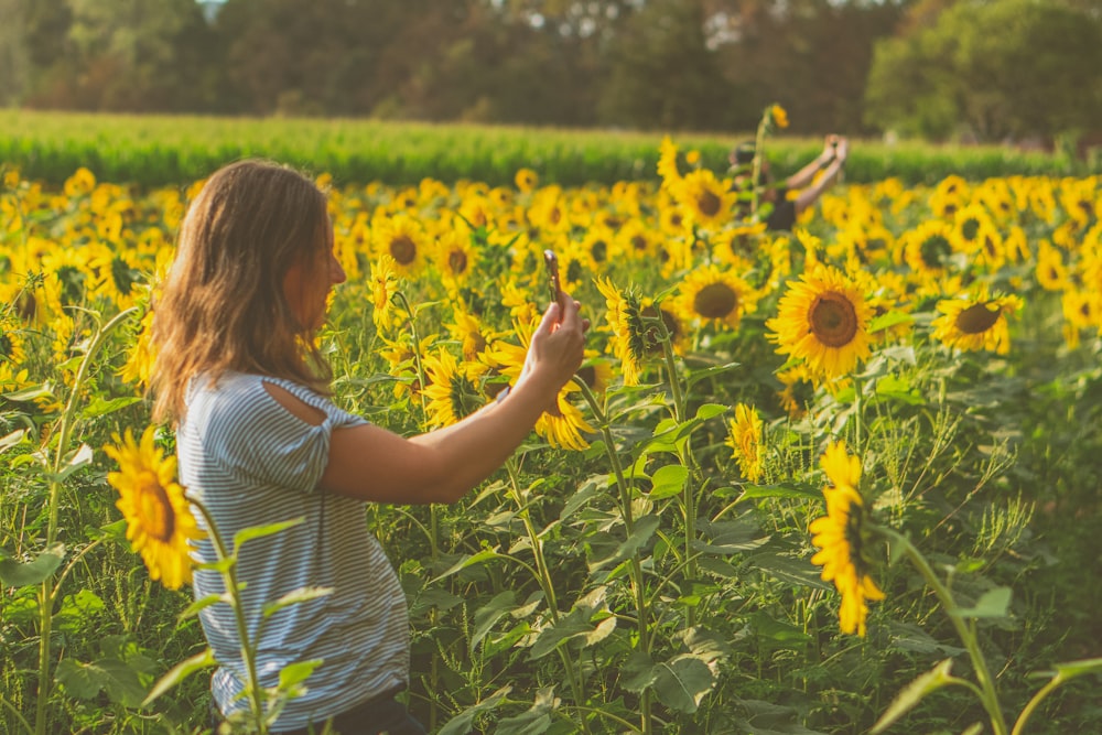 girl in white and black stripe tank top standing on sunflower field during daytime