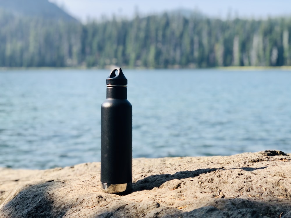 Botella deportiva negra y gris sobre arena marrón cerca del cuerpo de agua durante el día