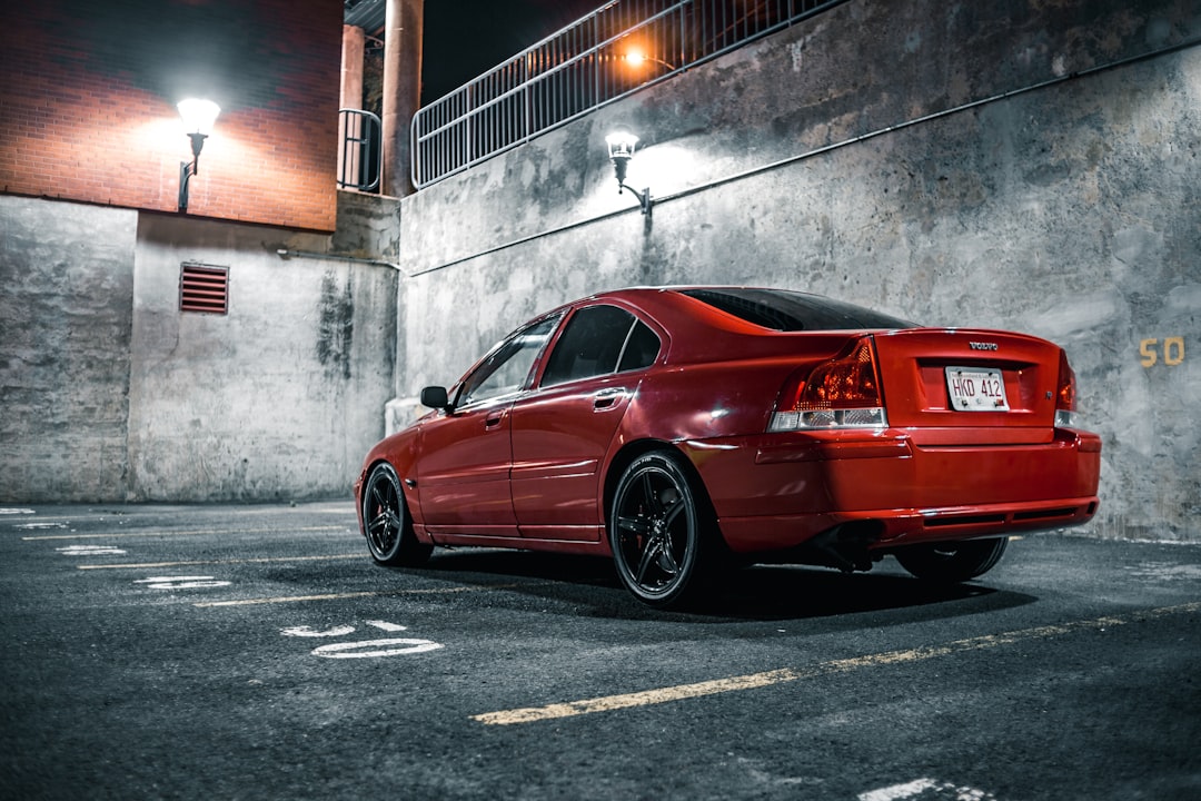 red coupe parked beside gray concrete wall