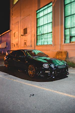 A sleek black sports car parked under city lights, with a content creator filming a dynamic shot nearby.