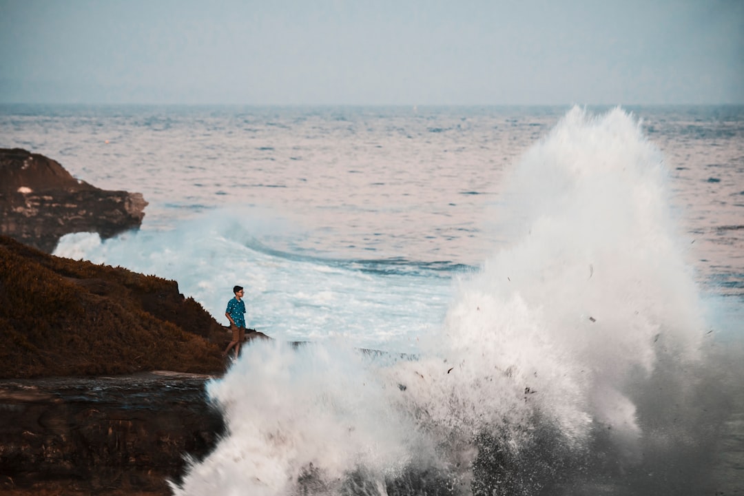 2 person standing on rock near sea waves during daytime