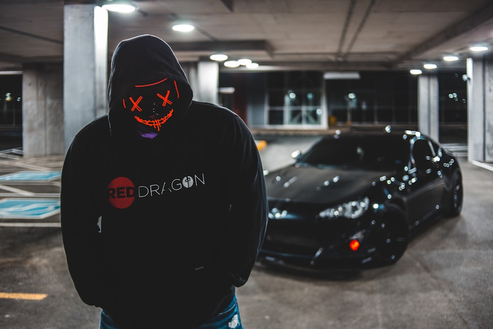 man in black hoodie standing beside black car