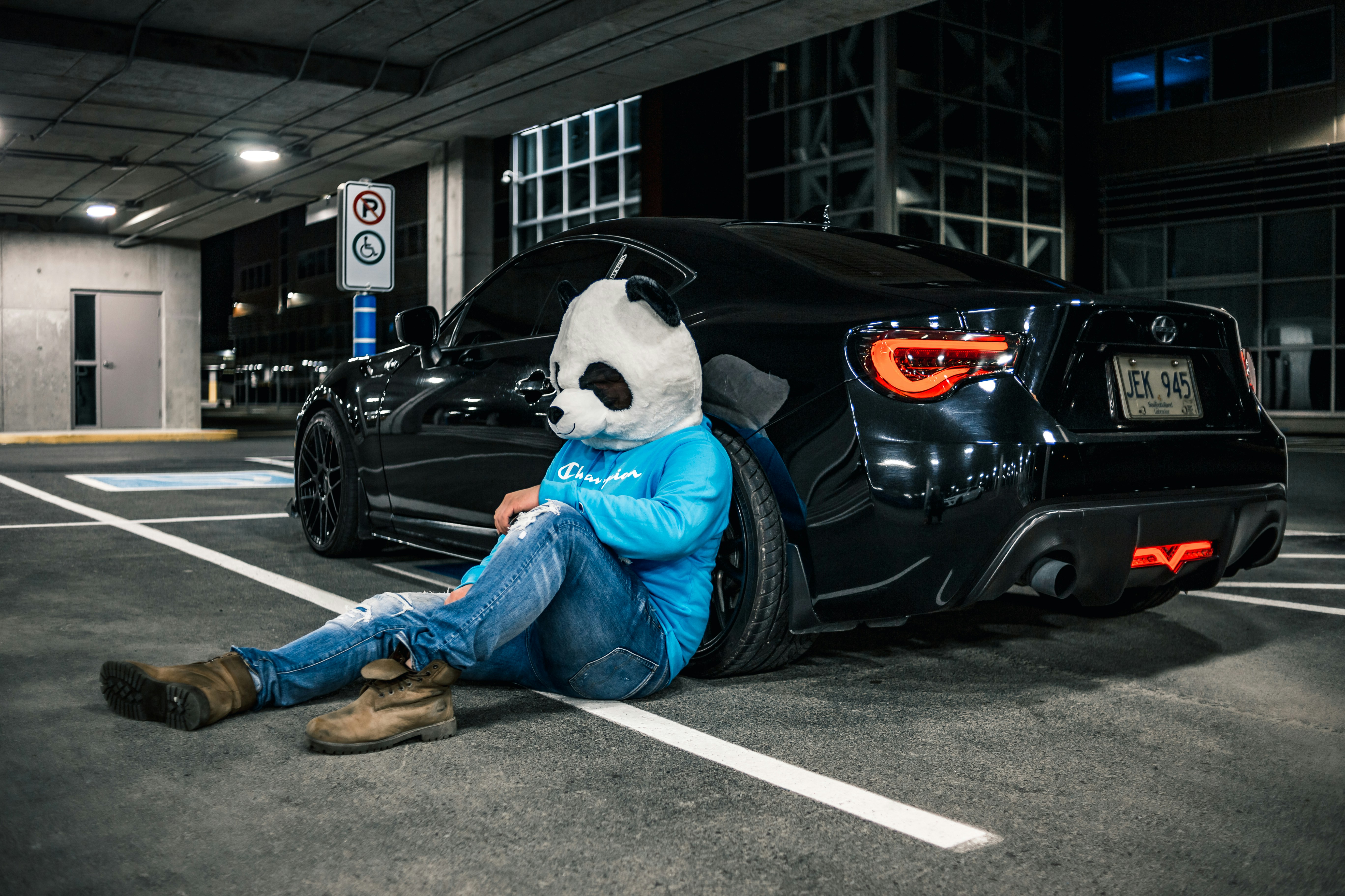 Orang dengan jeans denim biru dan topeng panda putih dan hitam duduk di kap mobil hitam