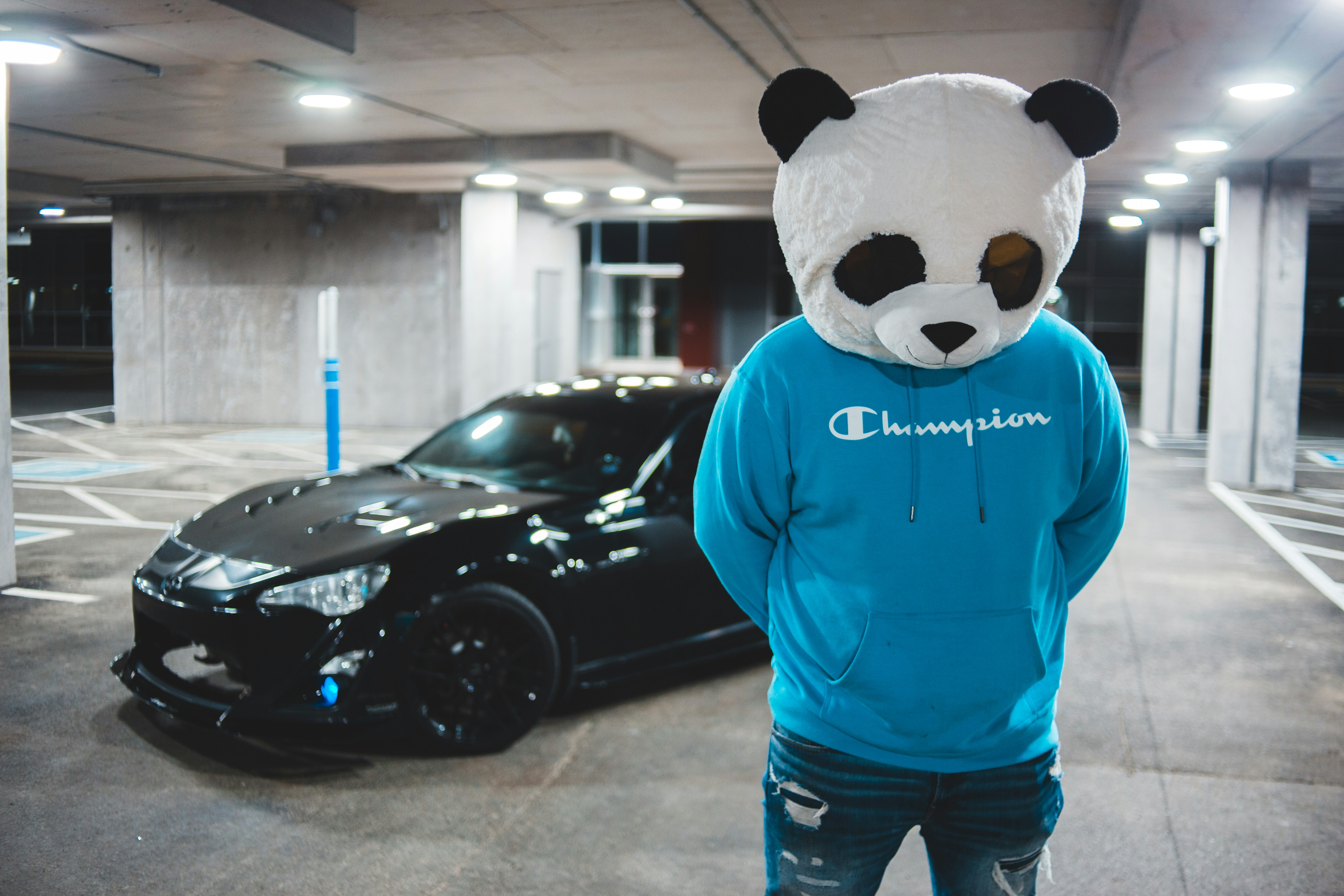 person in blue sweater and black and white panda mask standing beside black car