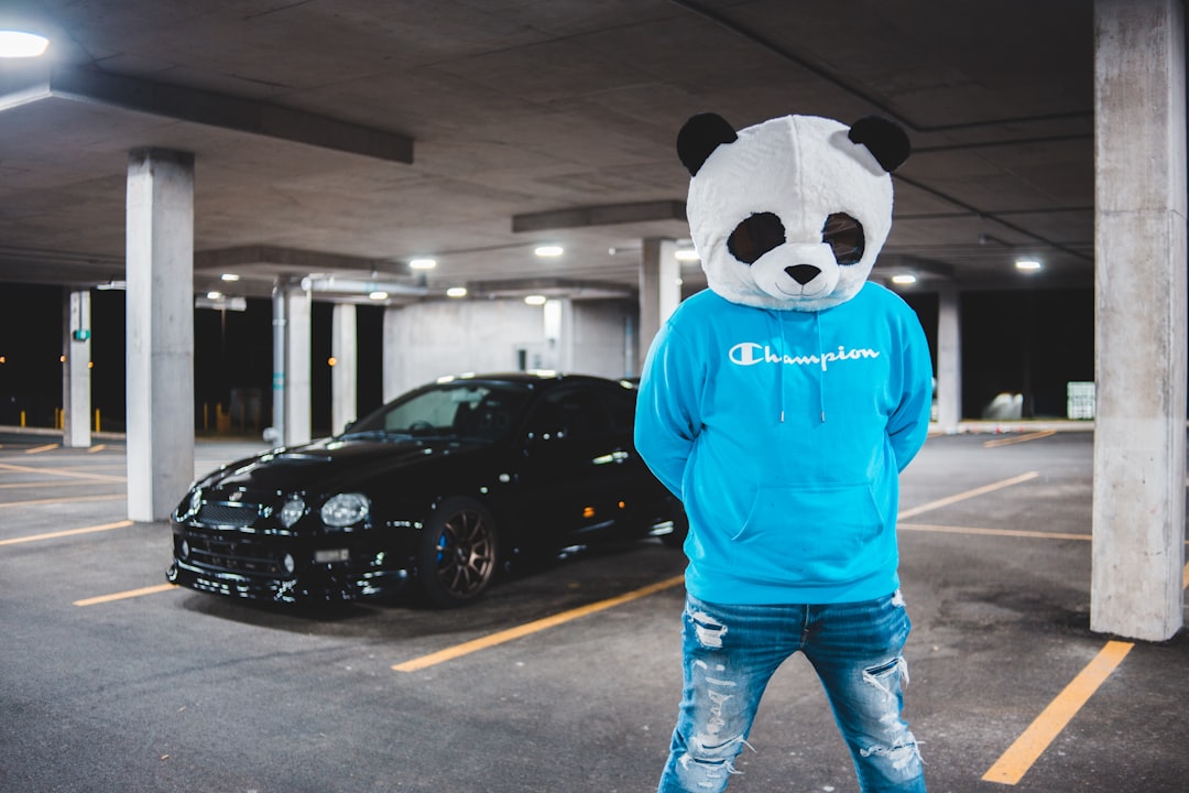 man in blue and white panda printed sweater and blue denim jeans standing on sidewalk during