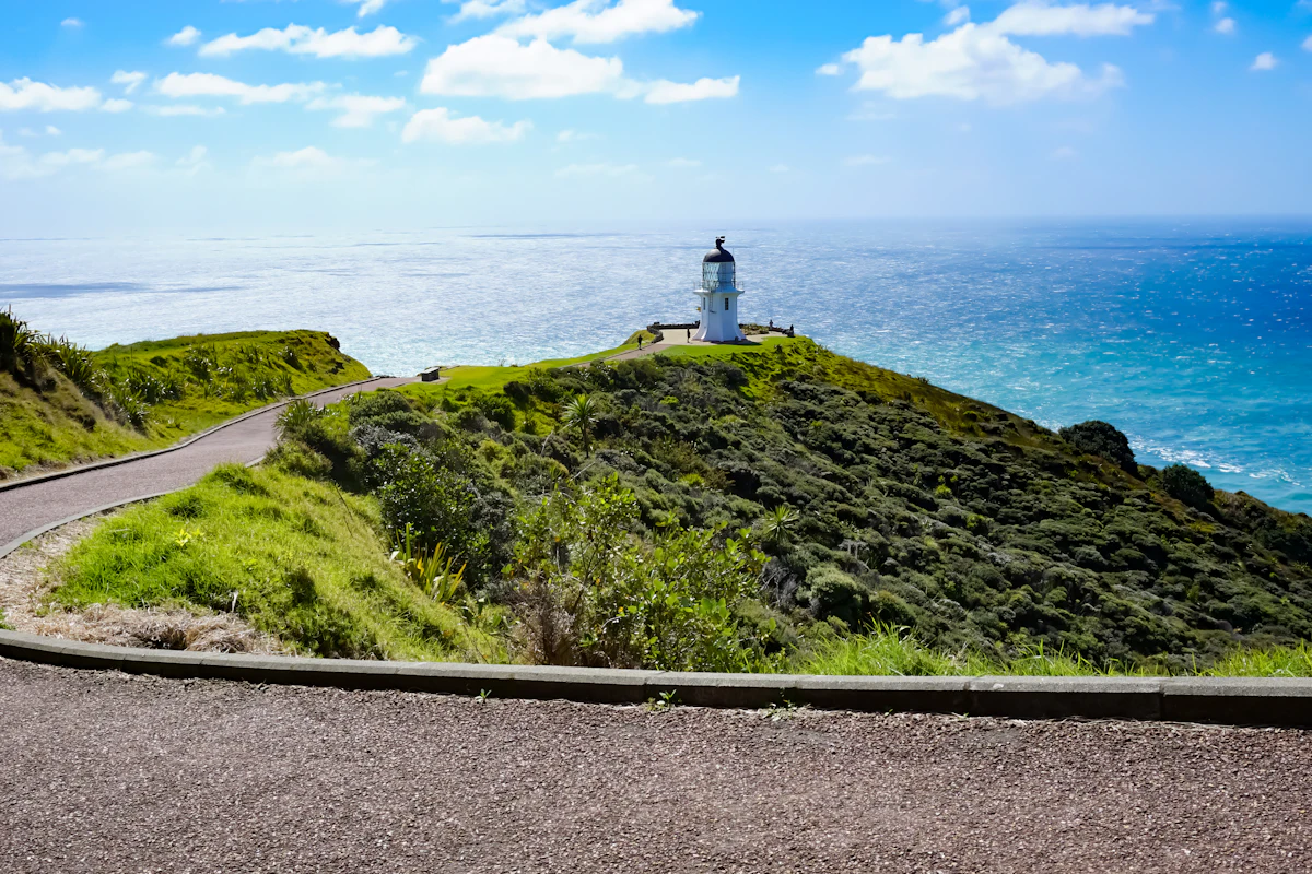 The white lighthouse at Cape Reinga on a green headland above the sea