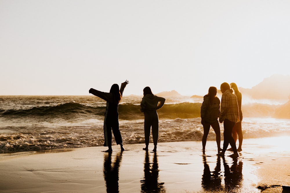 silhouette of 3 women and 2 men standing on beach during sunset