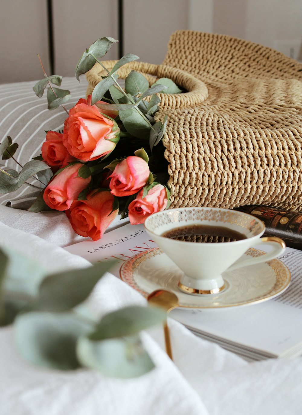 白いテーブルクロスに白い陶器のティーカップの横に赤いバラ