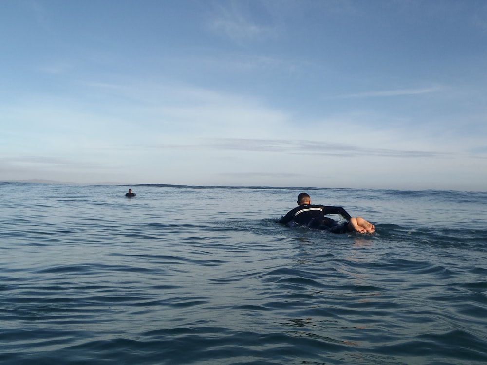 man in black wetsuit lying on blue sea under blue sky during daytime