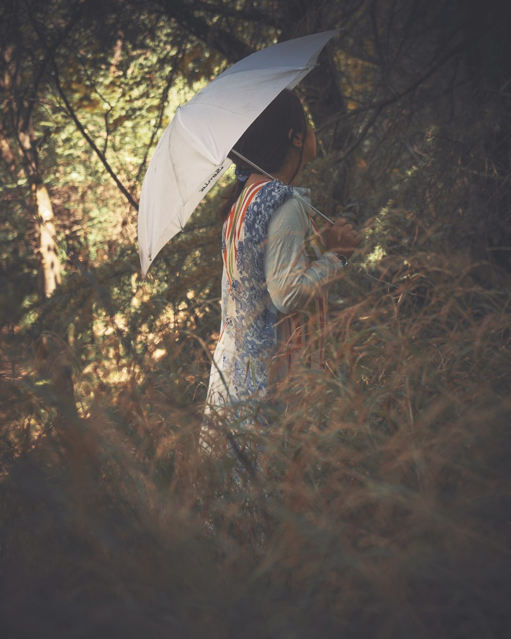 woman in white and black dress holding umbrella standing on dried leaves