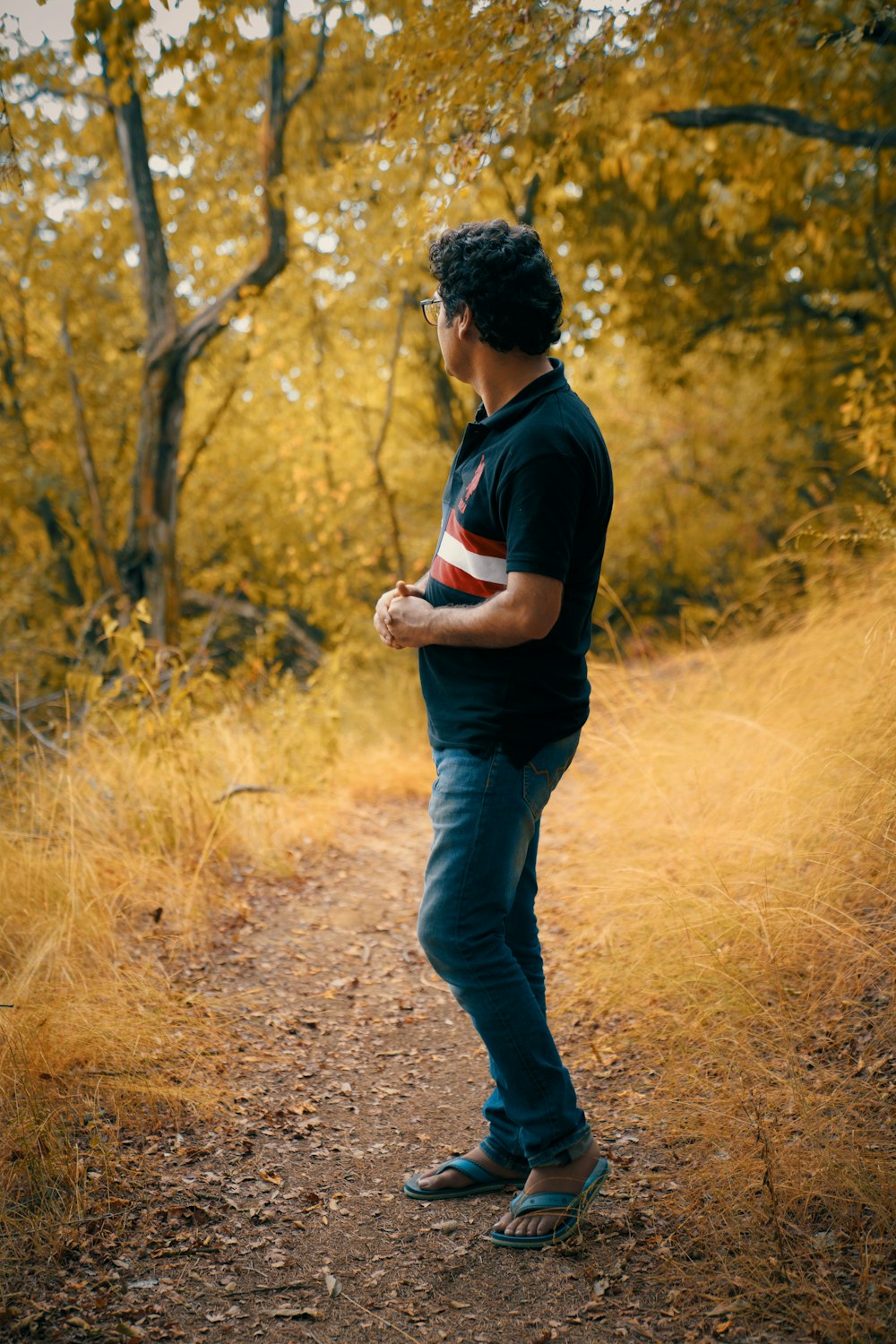 man in black shirt and blue denim jeans walking on dirt road during daytime
