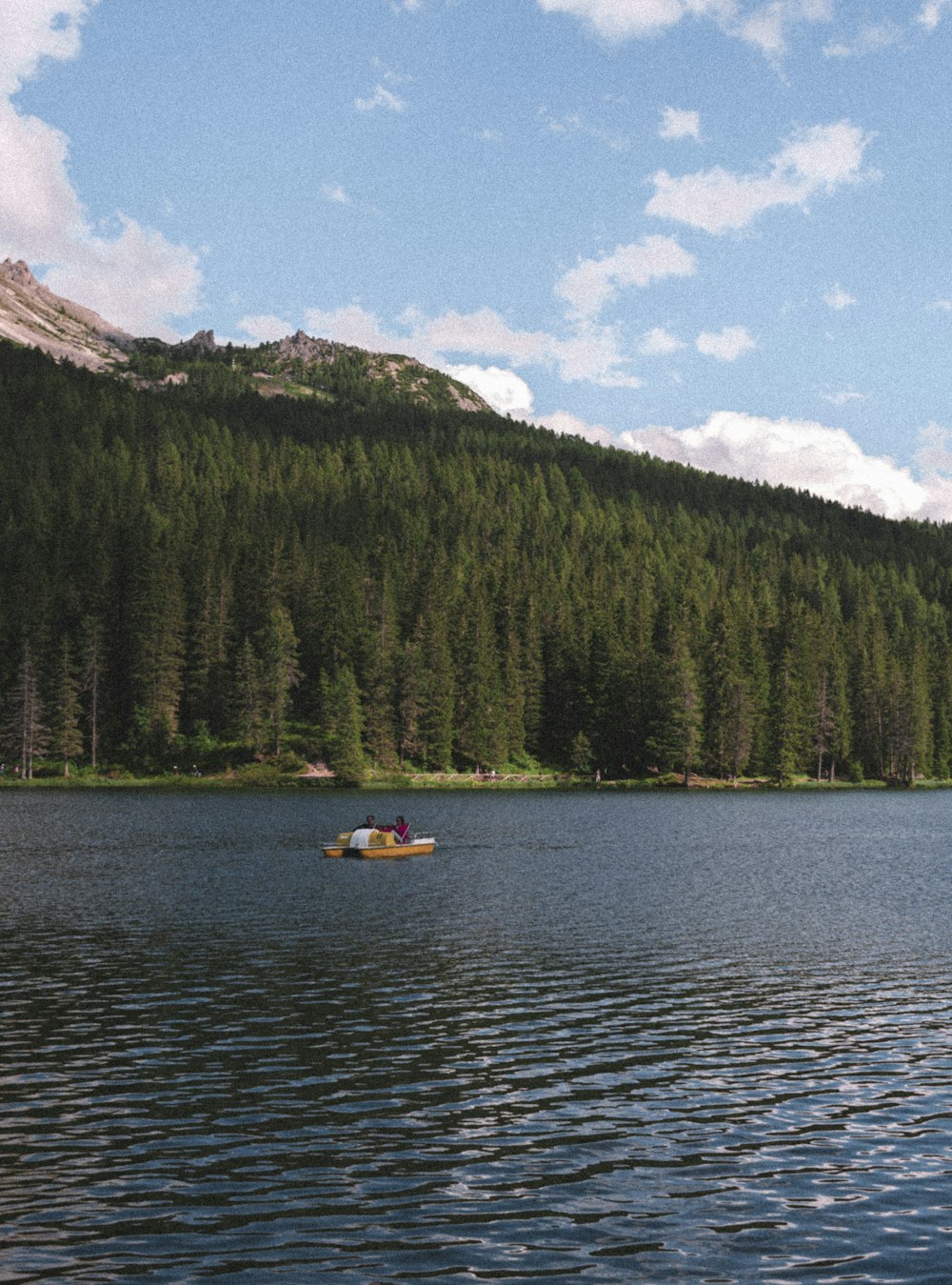 person riding on yellow kayak on lake near green trees and mountain during daytime